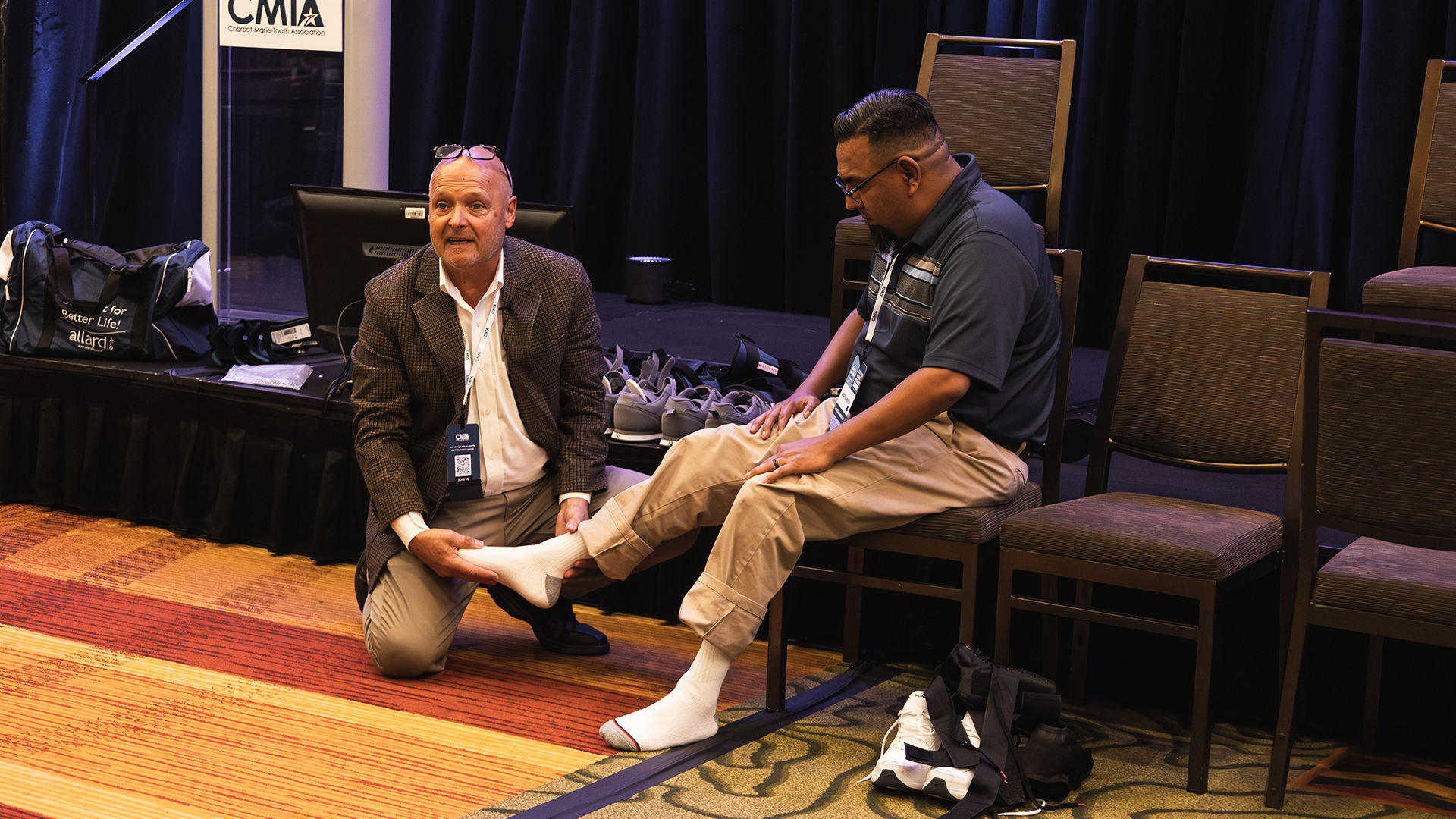 Ken Cornell speaking to audience while kneeling and holding a man's socked foot.