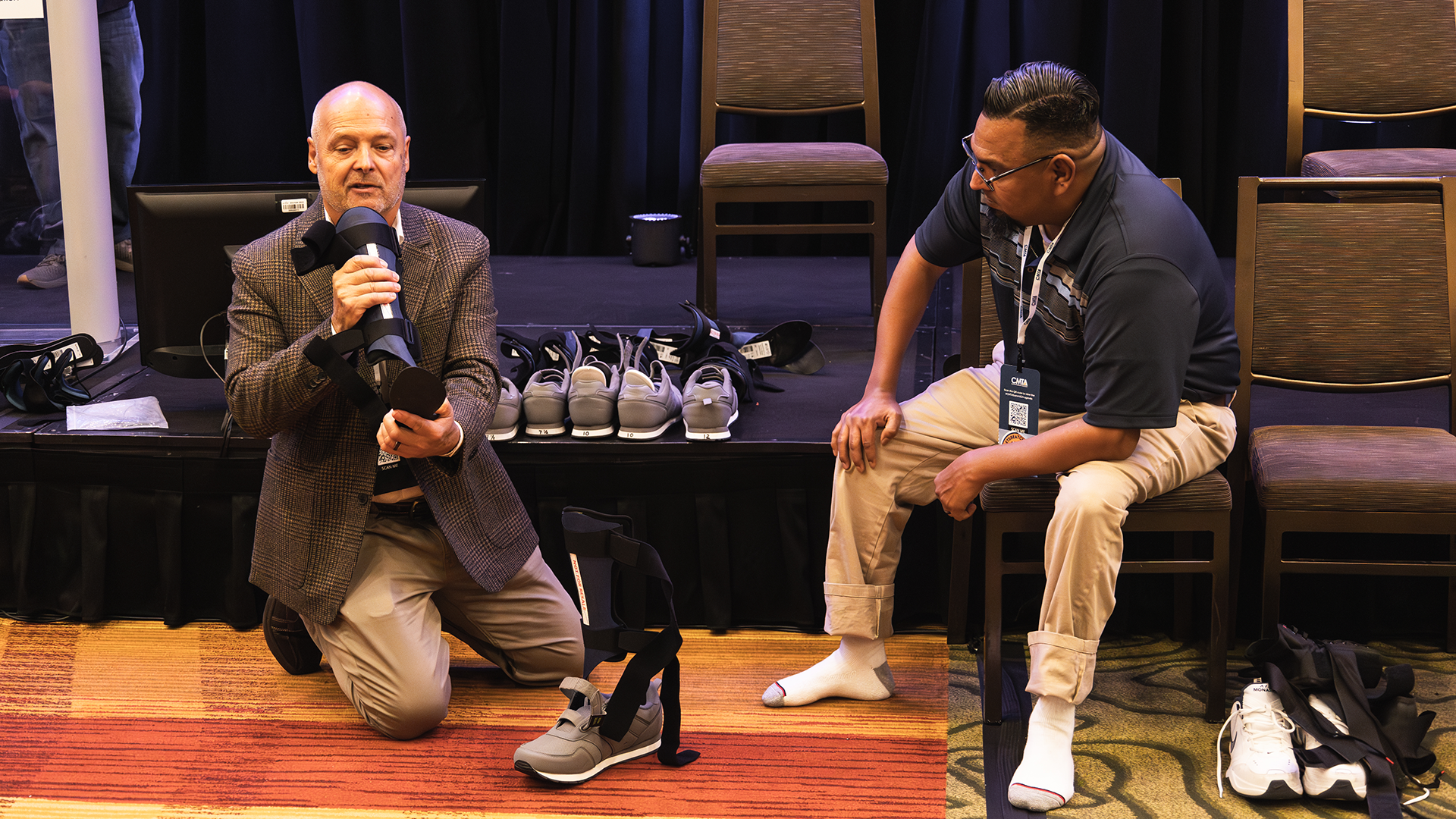 Ken Cornell presenting a foot brace while a seated man watches.
